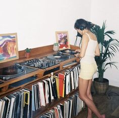 a woman standing in front of a record player on top of a wooden shelf filled with records