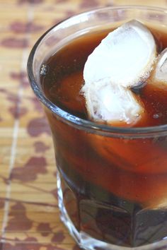 a glass filled with liquid and ice sitting on top of a wooden table next to a spoon