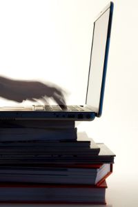 a person is typing on a laptop while sitting on top of stacks of folders