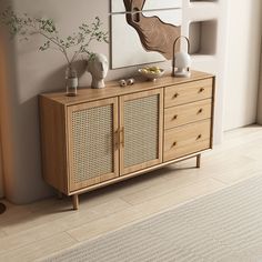 a wooden cabinet with wicker doors next to a painting and vases on the wall