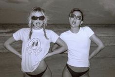 two women in bathing suits standing on the beach with their hands on their hipss