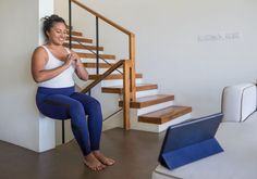 a woman sitting on the floor in front of a stair case with a laptop computer next to her