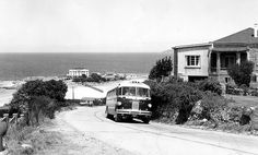 a black and white photo of a bus driving down the road next to some houses