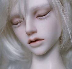 a close up of a white doll with blonde hair and eyes closed to the side