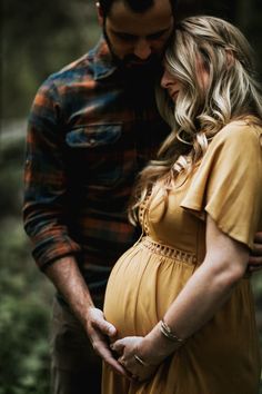 a pregnant couple cuddle in the woods