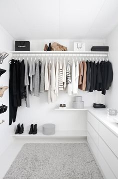 a white closet with clothes and shoes hanging on the wall next to a counter top