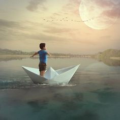 a boy standing on top of a paper boat in the water with birds flying overhead