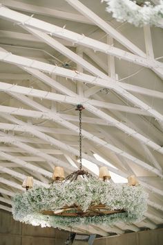 a chandelier hanging from the ceiling in a building with white beams and moss growing on it