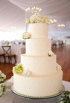 a wedding cake with white flowers on top is sitting on a table in a tent