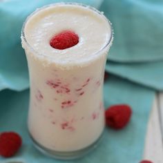 a glass filled with milk and raspberries on top of a blue cloth next to spoons