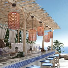 an outdoor bar with blue stools next to the ocean and hanging lights above it