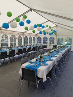 a large tent with tables and chairs set up for an event or party, decorated with blue and green paper lanterns