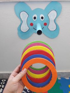 a person holding a stack of colorful rings in front of a wall with a paper cut out of an elephant on it