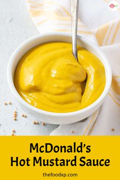 a white bowl filled with yellow mustard on top of a table next to a spoon