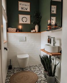 a white toilet sitting in a bathroom next to a sink under a mirror and potted plant