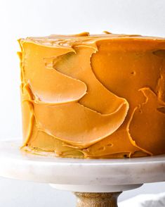 a close up of a cake with frosting on a white plate and a wooden stand