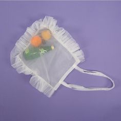 a plastic bag with two bottles in it on a purple surface, next to some oranges and an empty bottle