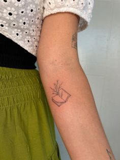 a person with a tattoo on their arm holding a book in one hand and a flower in the other