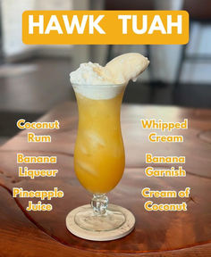 an orange drink sitting on top of a wooden table next to a sign that says hawk tuah