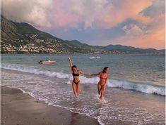 two women in bikinis are running into the water at the beach with their arms outstretched