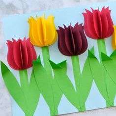 four paper flowers on a piece of white paper with green stems and red ones in the middle