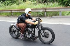 a man riding on the back of a motorcycle down a curvy road with trees in the background