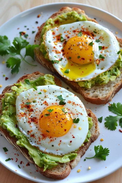 Two slices of avocado toast topped with fried eggs and a sprinkle of red seasoning, garnished with fresh cilantro leaves on a white plate. Avocado Toast Recipes With Egg, Healthy Vegetarian Recipes Breakfast, Breakfast Ideas Avocado Toast, Easy Breakfast Toast, Breakfasts With Avocado, Toppings For Toast, Romanticize Your Morning, Easy Breakfast Toast Ideas, Healthy Breakfast Avocado Toast