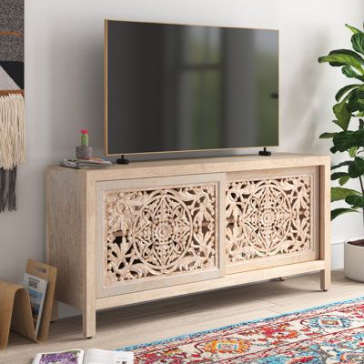 Bring boho-inspired style to your living room with this TV stand. Made from kiln-dried solid mango wood, it features a tan finish that highlights the wood's natural grain. It measures 68'' wide, so it accommodates TVs up to 75''. Two intricately carved doors showcase mandala-inspired botanical patterns, and they open up to reveal shelf space for books, baskets, and DVDs. Its light finish has just the right amount of distressing for a lived-in feel. Plus, a cable management cutout keeps pesky wir Home Tv Stand, Indian Living Rooms, Stands Tv, Wood Credenza, Wood Tv Stand, Solid Wood Tv Stand, Solid Wood Storage, Solid Wood Sideboard, Indian Furniture