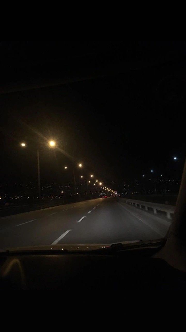 the dashboard of a car at night with street lights in the distance and dark sky