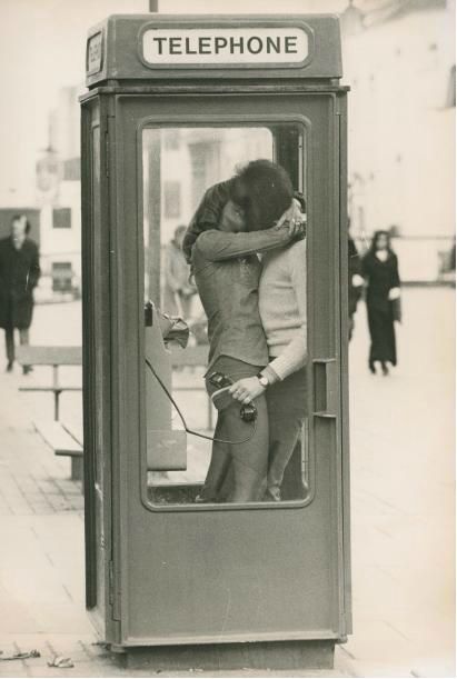 an old telephone booth with a man and woman in the phone booth hugging each other