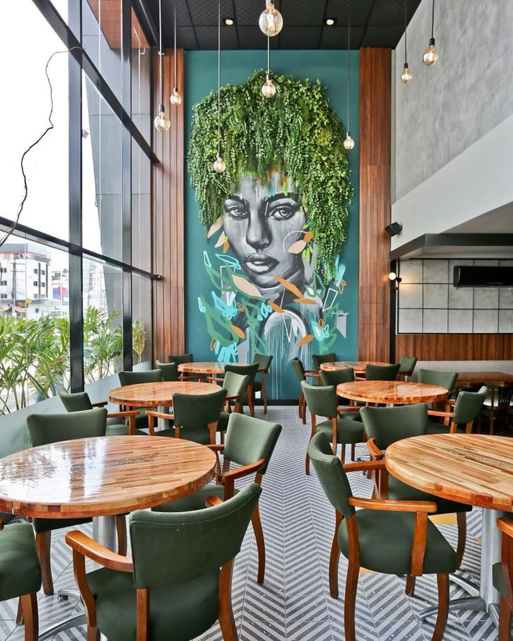 an empty restaurant with green chairs and wooden tables in front of a painting on the wall