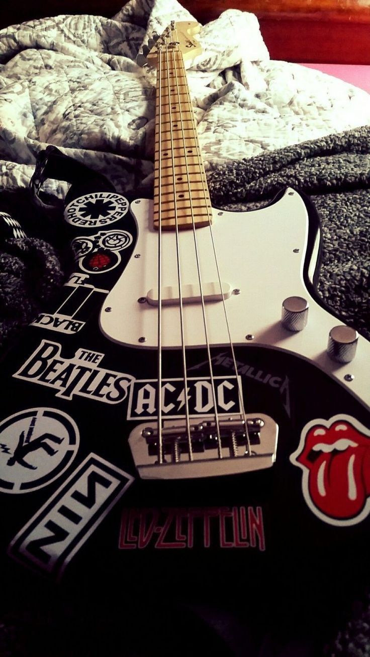 an electric guitar laying on top of a bed with stickers all over it's body