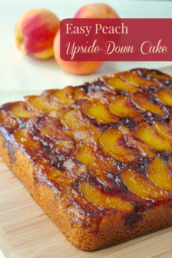 an upside down cake is sitting on a cutting board next to some peaches and apples