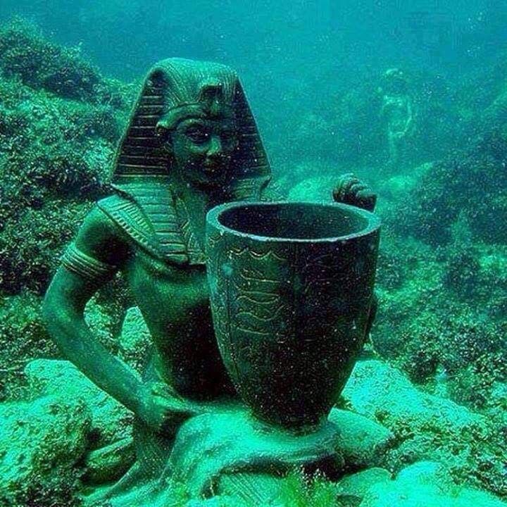 an ancient statue sitting on the bottom of a coral reef