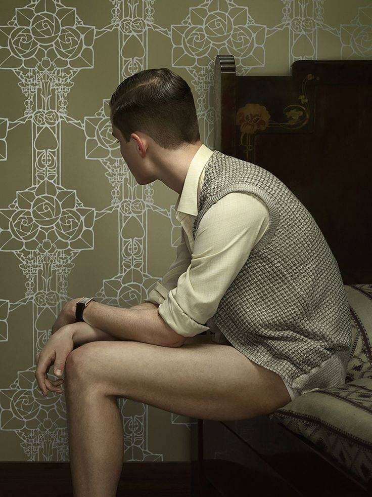 a man sitting on top of a bed in front of a wallpapered room