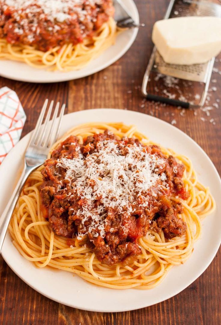 two plates of spaghetti with meat sauce and parmesan cheese on top, next to a grater