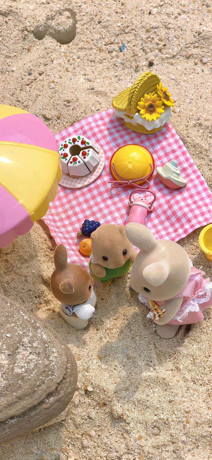 toy animals are sitting on the sand near a picnic table with an umbrella and sunflowers