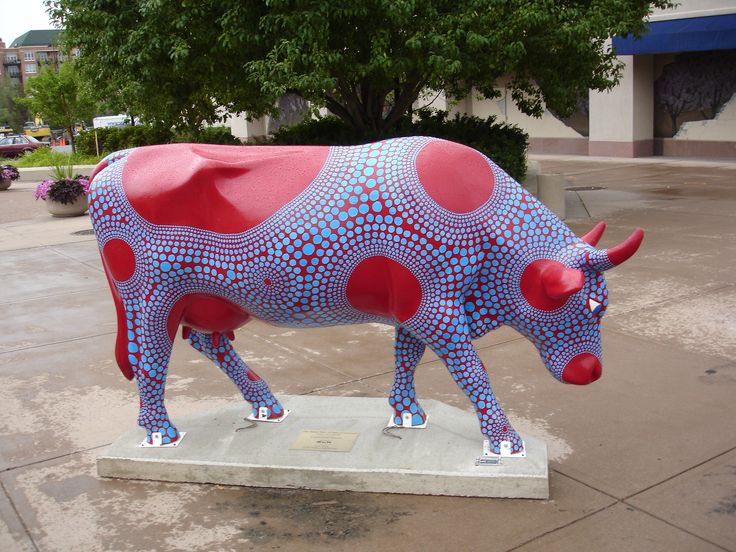 a red and blue cow statue sitting on top of a cement slab