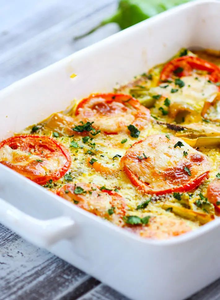 a casserole dish with tomatoes, cheese and herbs in it on a wooden table