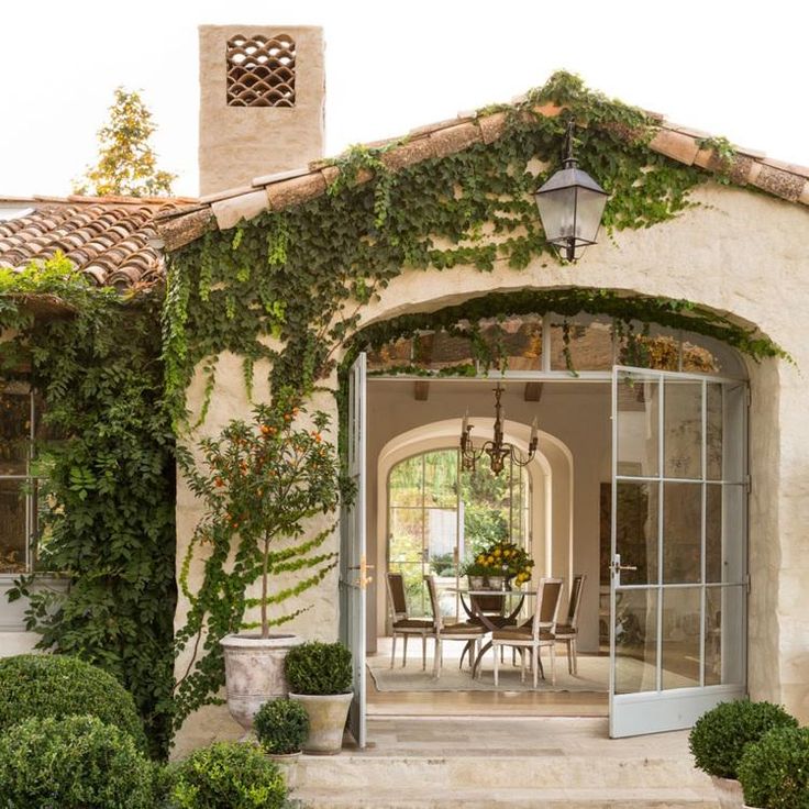 an outdoor dining area with potted plants and greenery on the side of a house