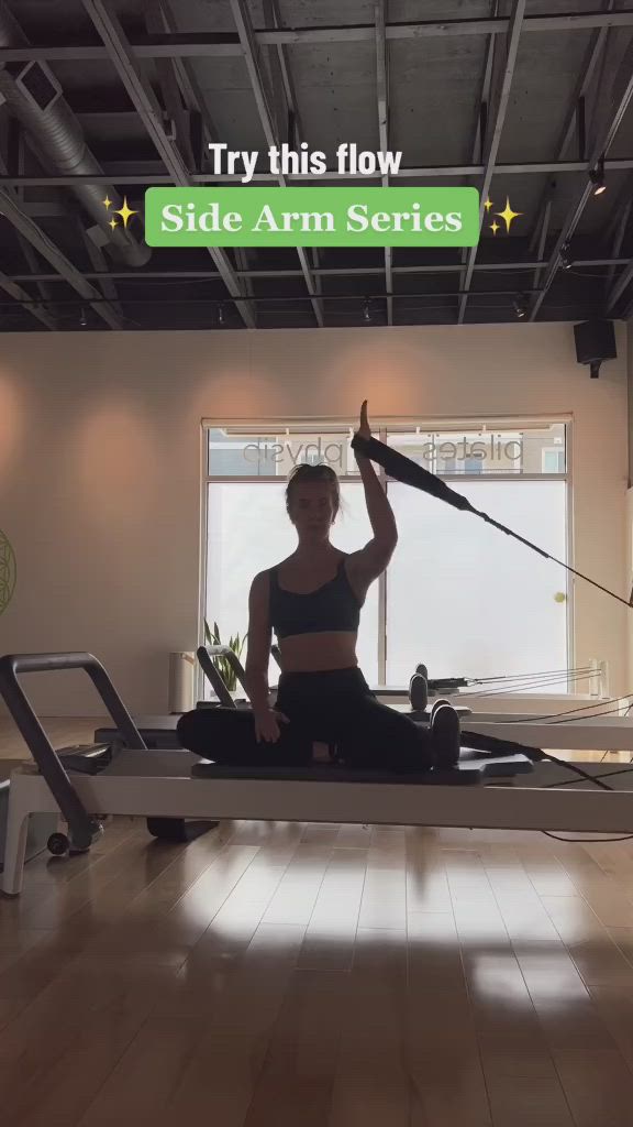 This may contain: a woman is sitting on a rowing machine with her arms in the air and holding a pole above her head