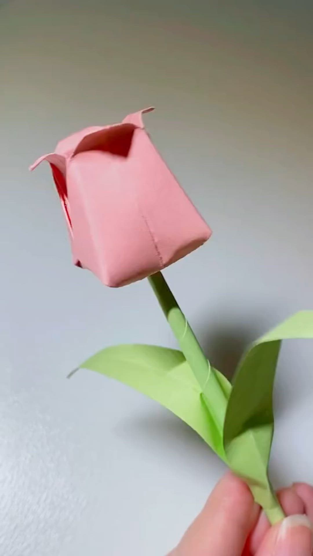 This may contain: a hand holding a pink origami flower