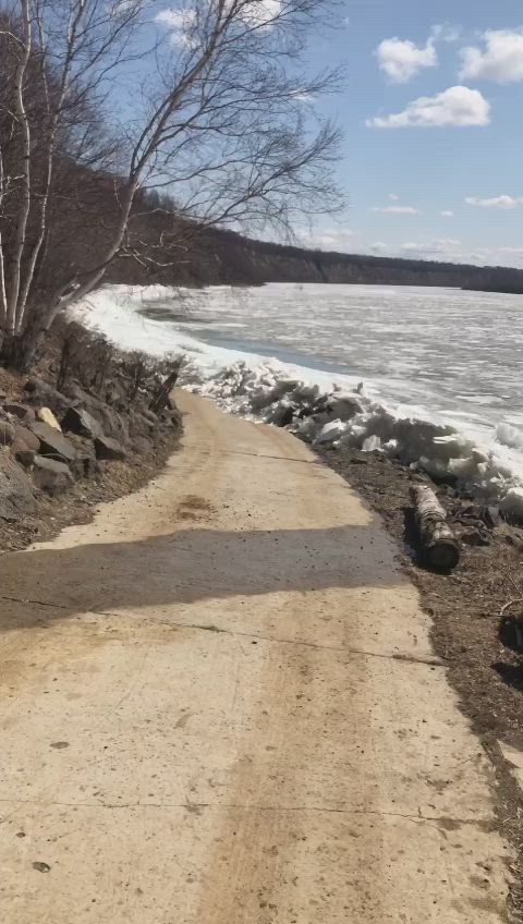 This may contain: a dirt road next to the water with ice on it