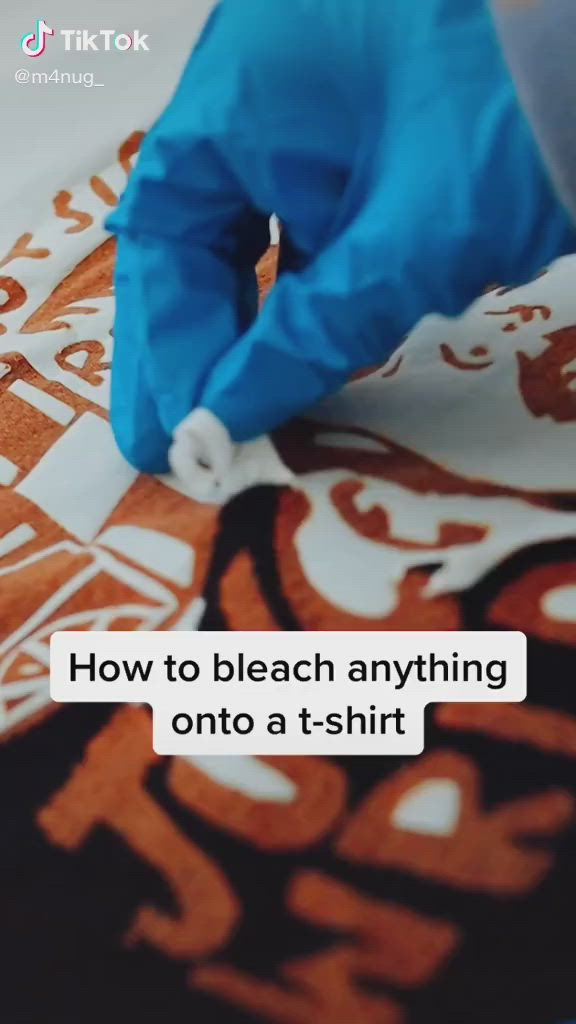 This may contain: someone in blue gloves is cutting up an orange and white fabric with scissors on it