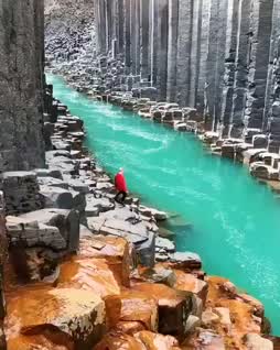 This may contain: a man standing in the middle of a river surrounded by large rock formations and green water