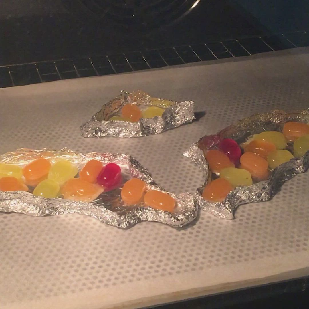 This may contain: two pieces of tin foil with gummy bears on top of it in an oven