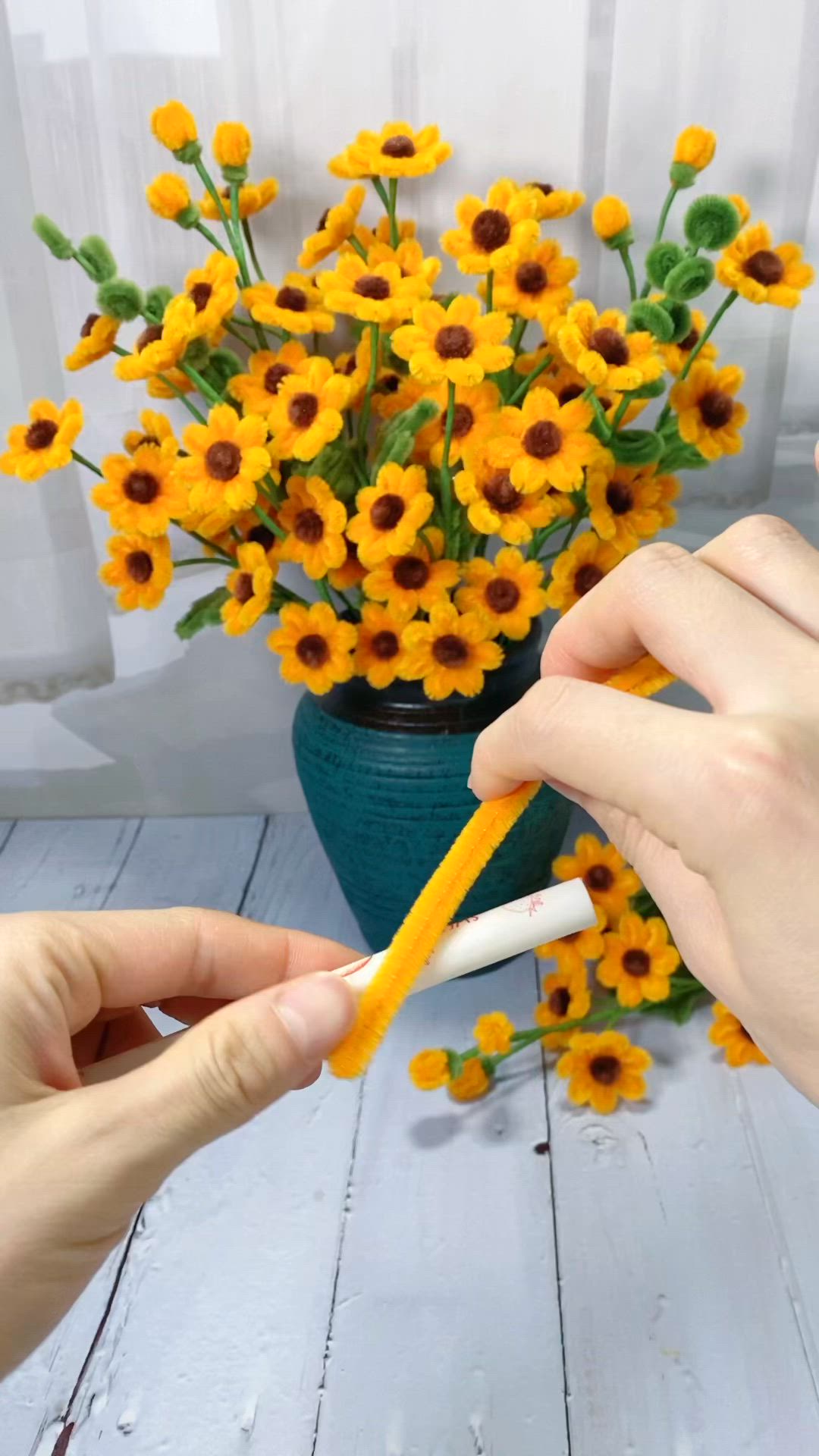 This may contain: two hands are holding an object near a vase with yellow flowers in it on a white wooden table