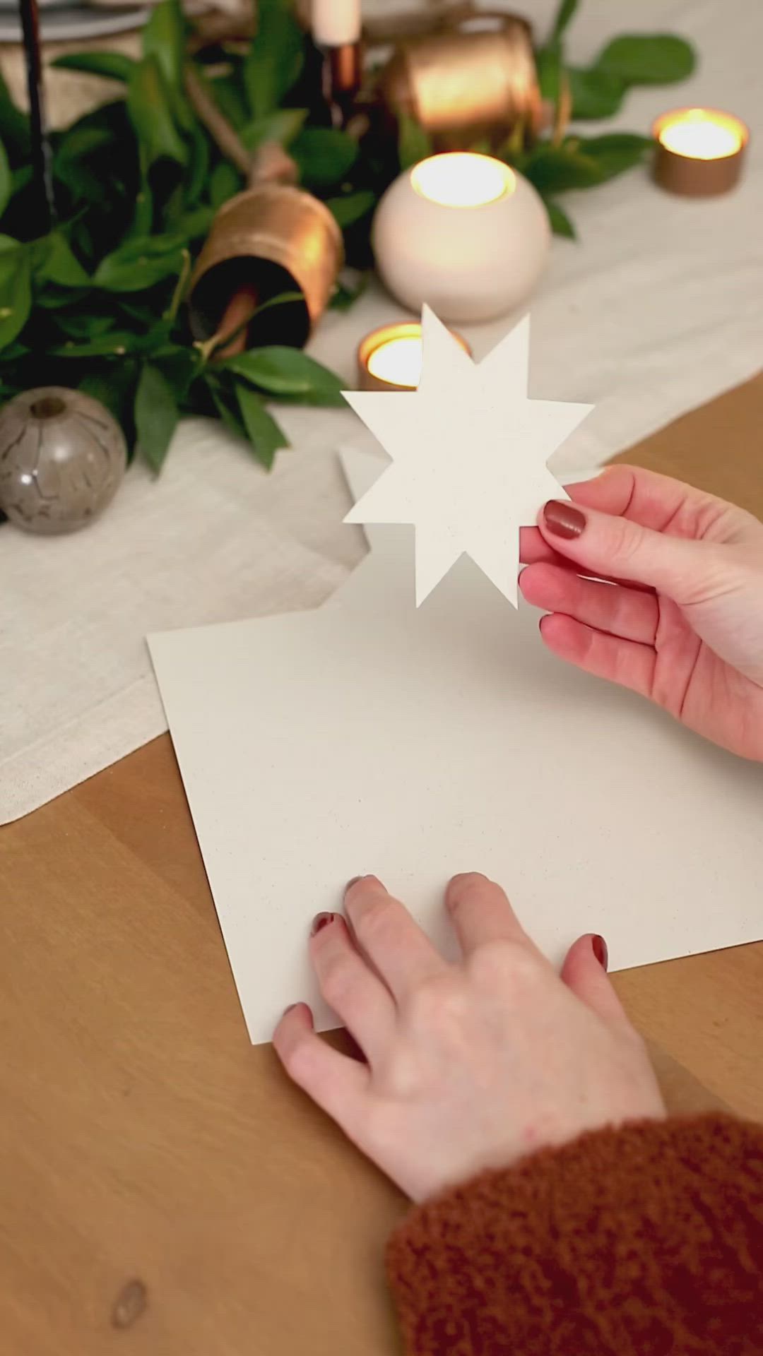 This may contain: a person is holding a paper flower on a table with candles and greenery in the background