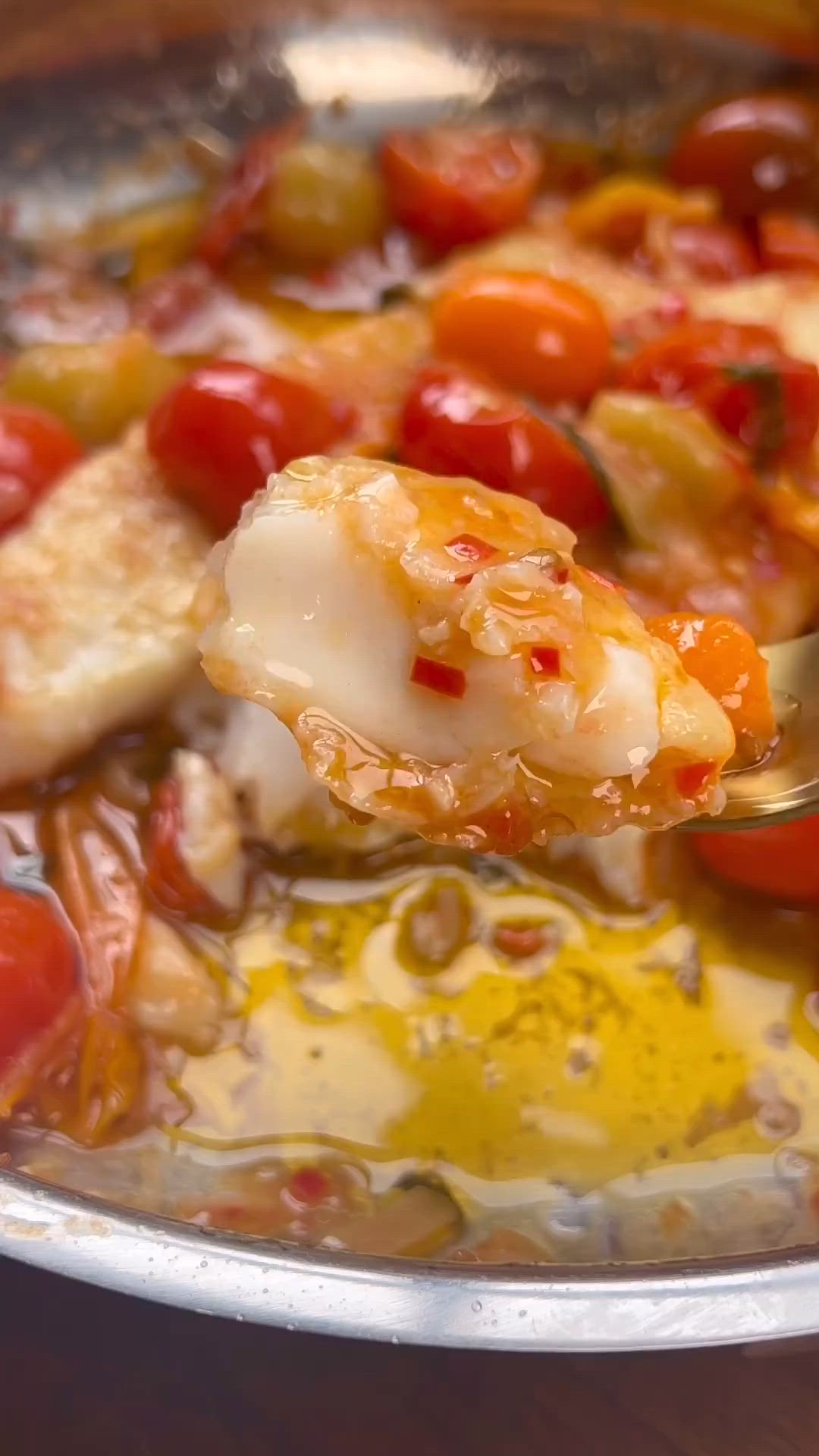 This may contain: a pan filled with fish and tomatoes on top of a table