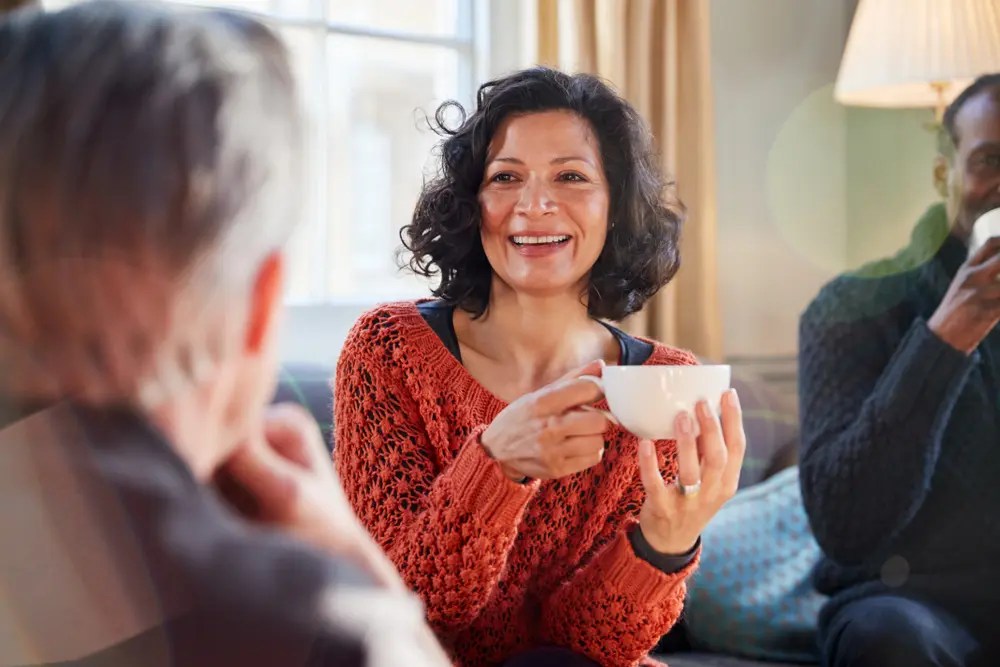 middle age woman sitting on a couch drinking coffee with friends